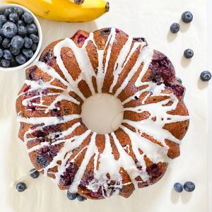 blueberry banana bread on white table with bananas and blueberries